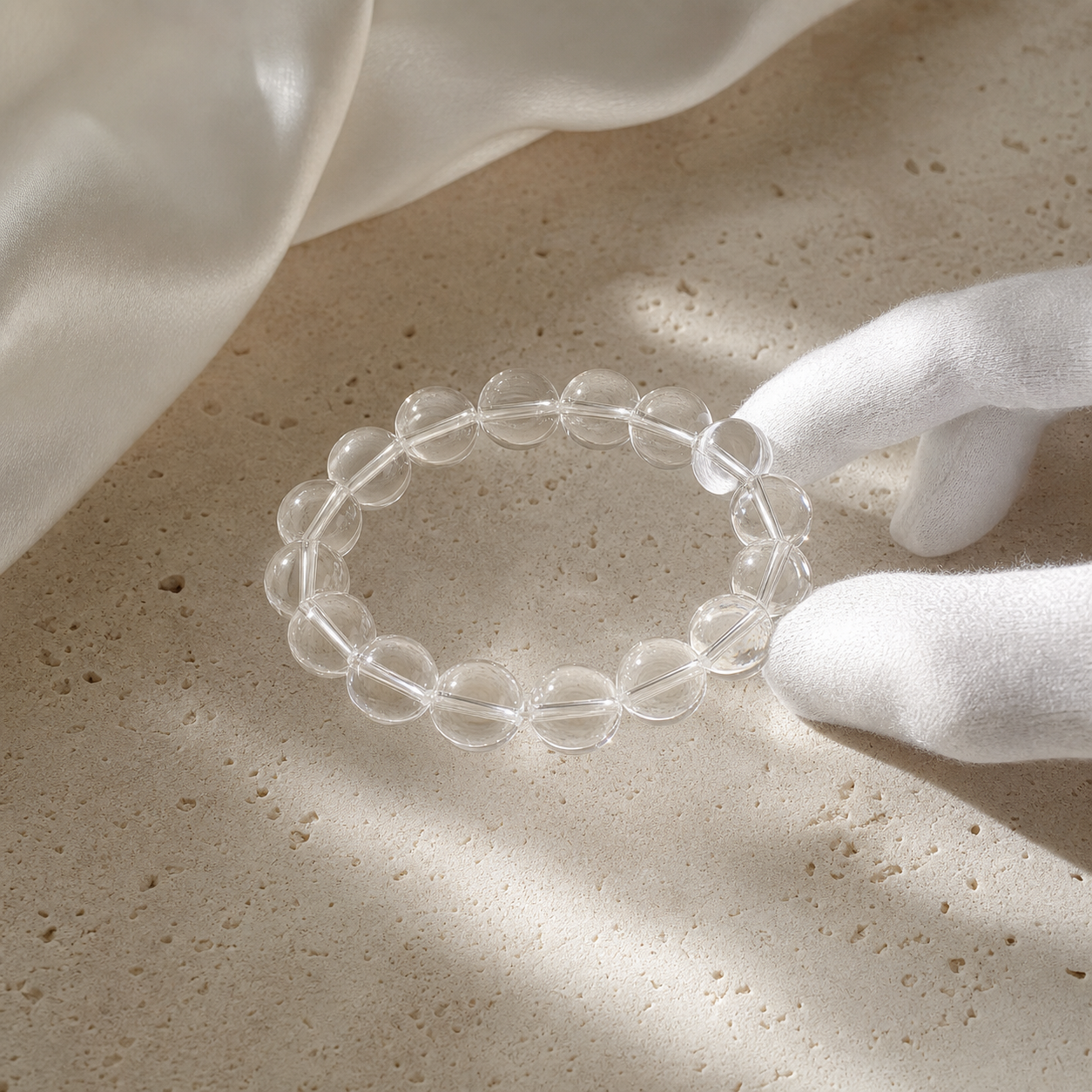 Clear quartz bracelet held with white gloves on natural stone
