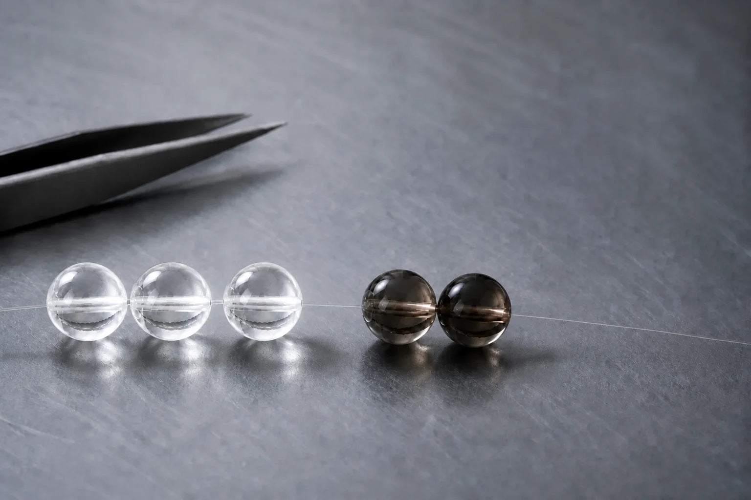 Full-size clear and smoky quartz beads beside precision tweezers